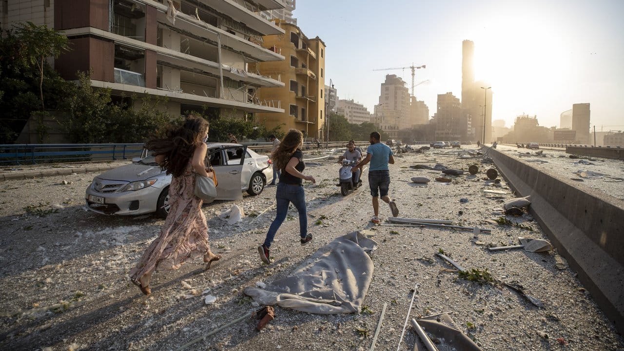 Menschen laufen nach der Explosion über eine von Trümmern übersäte Straße.