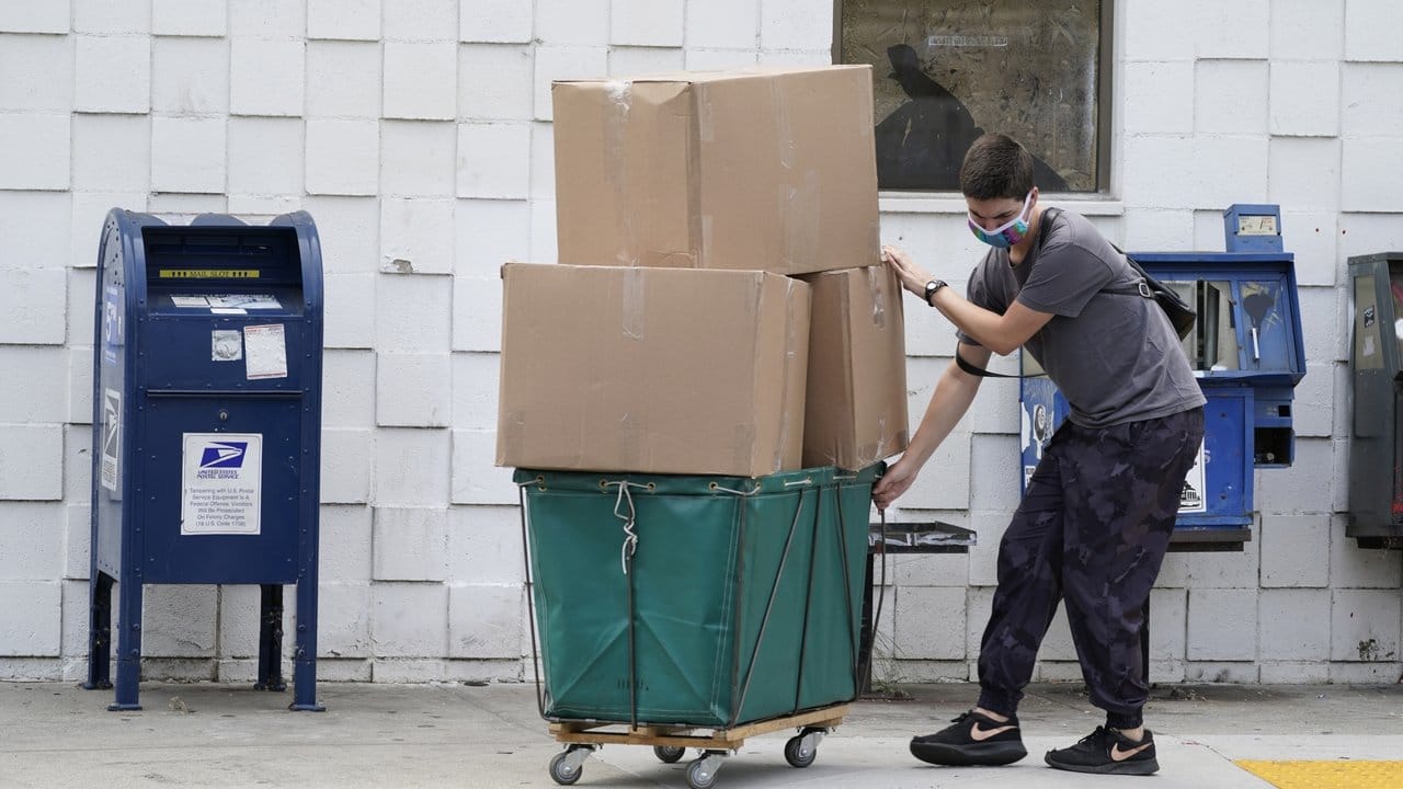 Ein Mann trägt eine Schutzmaske während er große Paketboxen von einem Postamt in Los Angeles in ein Fahrzeug transportiert.
