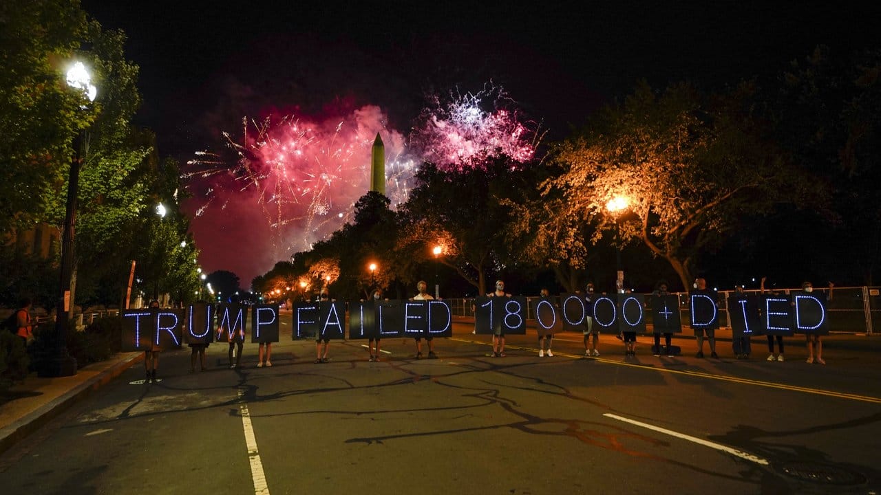 Demonstranten halten Schilder auf denen Leuchtdioden eine Botschaft bilden, während ein Feuerwerk den Himmel um das Washington Monument erhellt, welches zum Abschluss des Parteitages der Republikaner gezündet wird.