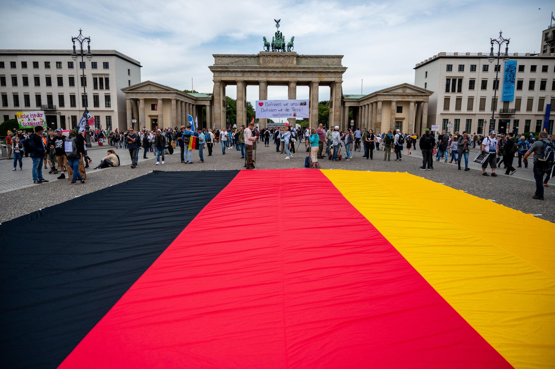 Vor dem Brandenburger Tor sind am Samstagvormittag Demonstranten zu sehen. Eine große Deutschlandflagge ist auf dem Boden ausgebreitet.
