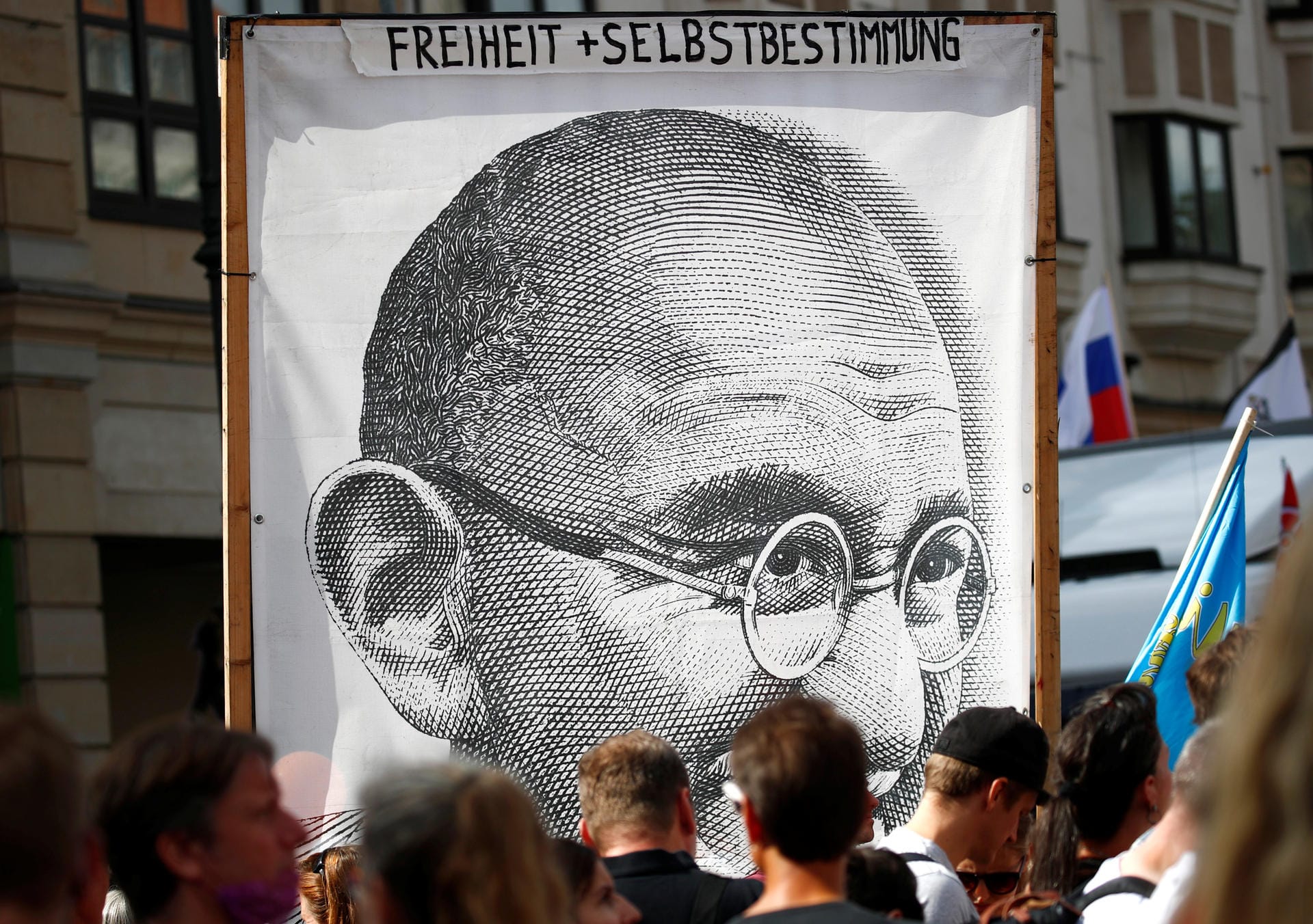 Demonstranten halten ein Porträt von Mahatma Gandhi hoch mit den Worten "Freiheit + Selbstbestimmung".