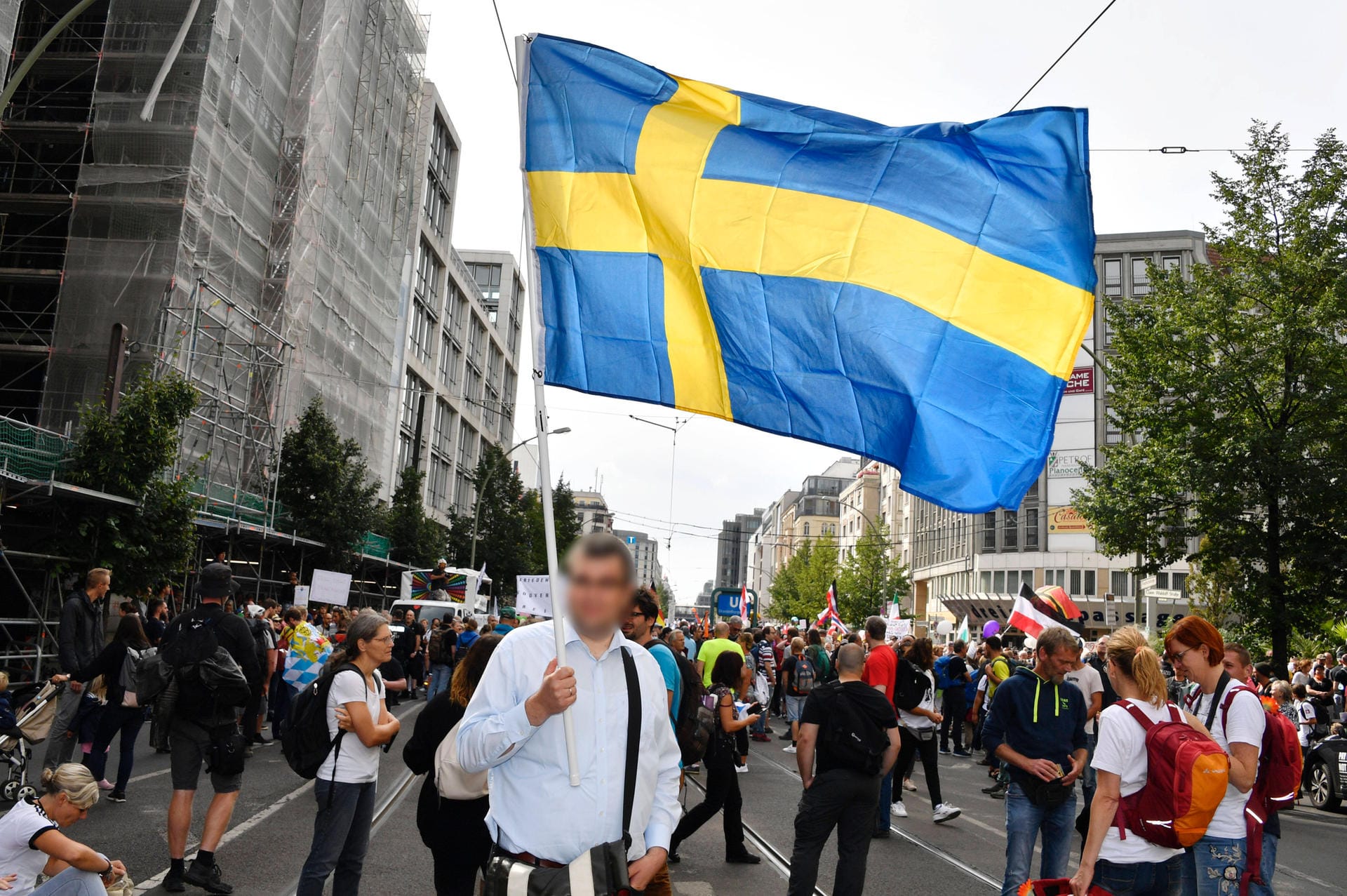Auch die Schwedische Flagge weht mit: Sie steht für den Sonderweg Schwedens. Trotz der steigenden Fallzahlen, wird der Umgang der schwedischen Regierung, mit der Corona-Pandemie, von den Demonstrierenden befürwortet.