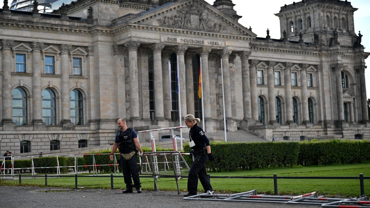 Ein Polizist und eine Polizistin tragen eine Absperrung am Reichstagsgebäude weg.