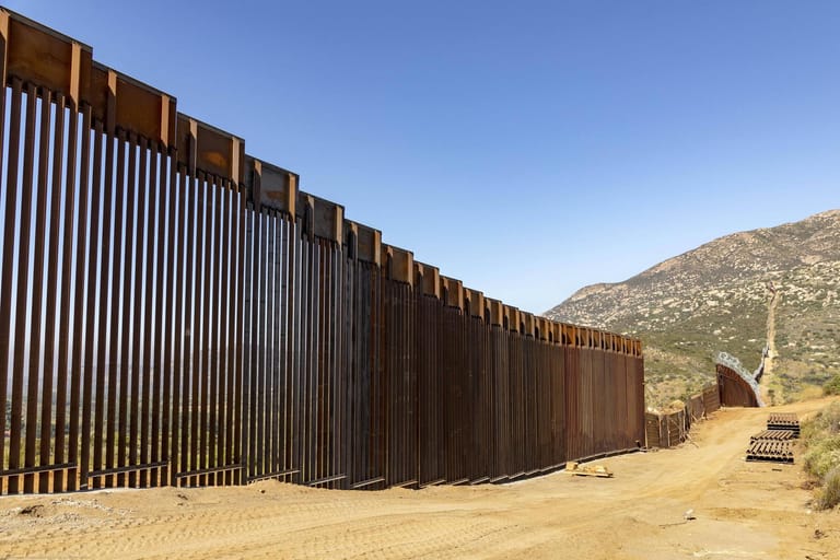 An der Grenzmauer zu Mexiko entzweien sich nicht nur die Geister, sondern auch Familien. Sie steht stellvertretend für die Flüchtlingspolitik der USA, welche schon vor der Amtszeit Trumps als hart galt. Die komplette Fertigstellung der 1.600 Kilometer langen Mauer scheitert bislang an Plan und Finanzierung. Diese solle, so Trump, Mexiko bezahlen.