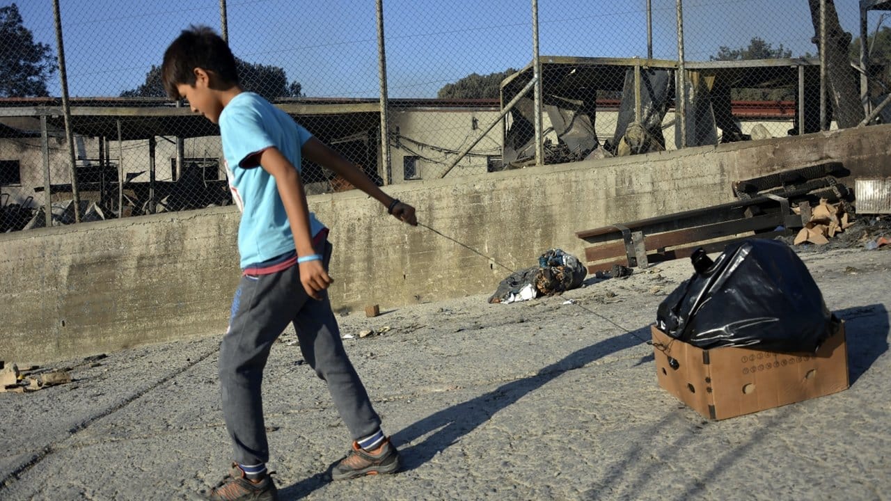 Ein Junge zieht nach dem Brand im Flüchtlingslager einen Karton mit einer Plastiktüte hinter sich her.