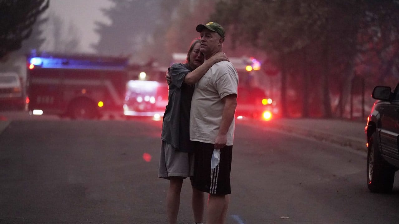 Ein Paar umarmt sich in Phoenix im US-Bundesstaat Oregon, während hinter ihm Feuerwehrwagen stehen.