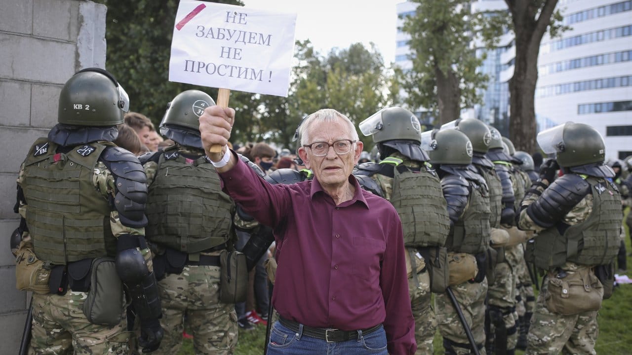 Ein älterer Demonstrant steht bei einem Protest der belarussischen Opposition gegen die Ergebnisse der Präsidentenwahl vor einer Gruppe von Polizisten und hält ein Schild mit der Aufschrift "Wir werden nicht vergessen, wir werden nicht verzeihen" in der Hand.