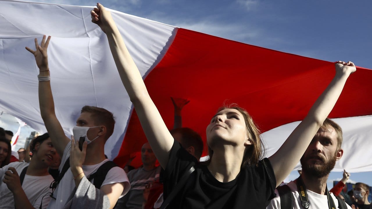 Demonstrantinnen und Demonstranten halten eine historische belarussische Flagge und nehmen an einem Protest der Opposition in Minsk teil.