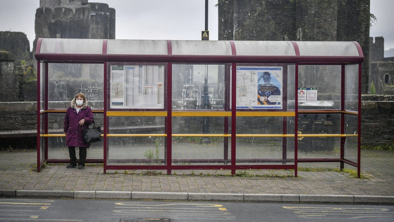 Eine Frau mit Mundschutz wartet in Caerphilly an einer Haltestelle auf den Bus.