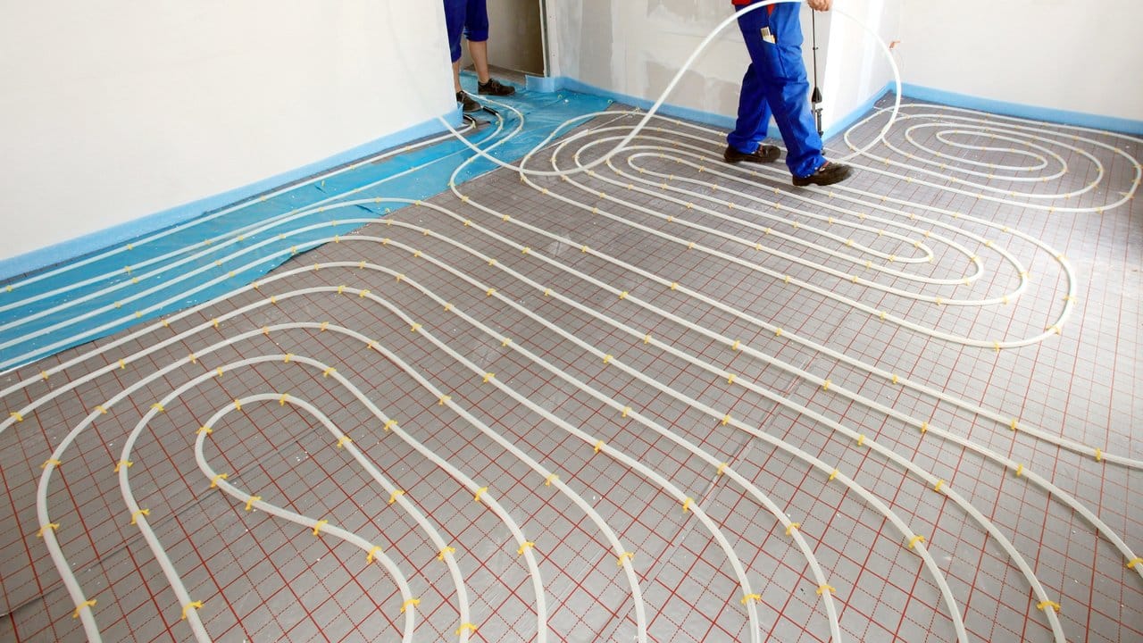Bei der Installation einer Fußbodenheizung werden Schläuche mit Hilfe eines Tackers auf Dämmplatten verlegt, darüber kommt Estrich.