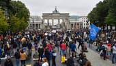 Berlin: Protestierende sitzen vor dem Brandenburger Tor am Boden. Zuvor wurden auf dem Asphalt Punkte markiert, auf denen sich die Teilnehmenden niederlassen sollten, um den Abstand einzuhalten.