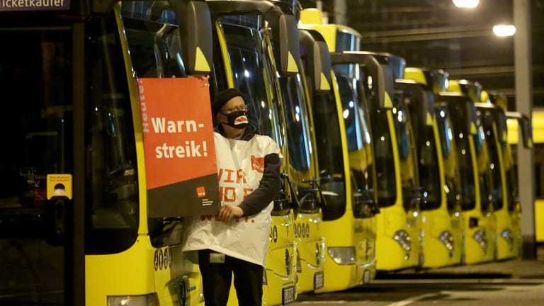 Ein streikender Busfahrer der Ruhrbahn klebt ein Plakat "Warnstreik" an einen Bus.