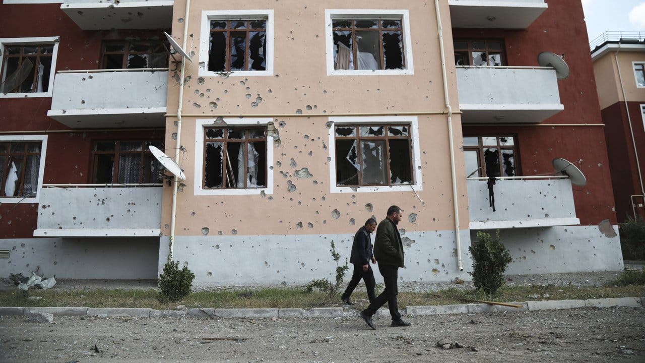 Zwei Männer gehen nach einem Beschuss der armenischen Artillerie an einem beschädigten Gebäude vorüber.