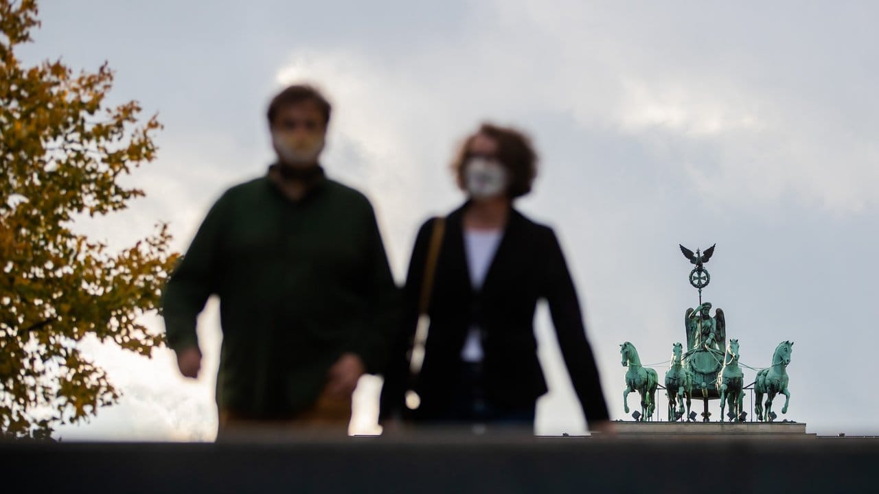 Ein Mann und eine Frau mit Mund-Nasen-Schutz vor der Quadriga des Brandenburger Tores in Berlin.