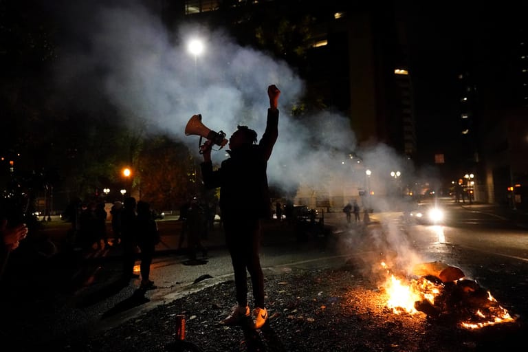 USA, Portland: Ein Demonstrant steht neben einer brennenden US-Flagge nach einem Protestmarsch in der Wahlnacht.