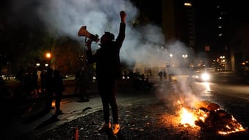 USA, Portland: Ein Demonstrant steht neben einer brennenden US-Flagge nach einem Protestmarsch in der Wahlnacht.