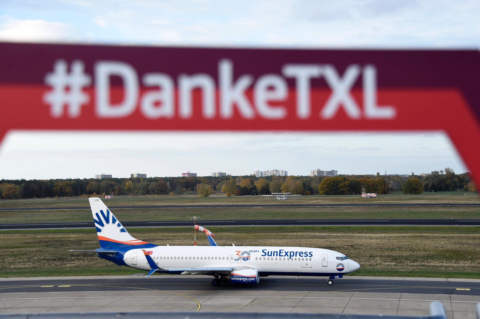 Eine Maschine fährt im November 2020 über das Rollfeld, darüber ist ein Schild mit einer Aufschrift zu sehen: Unter dem Hashtag "DankeTXL" verabschieden sich Fans vom Flughafen Berlin-Tegel.