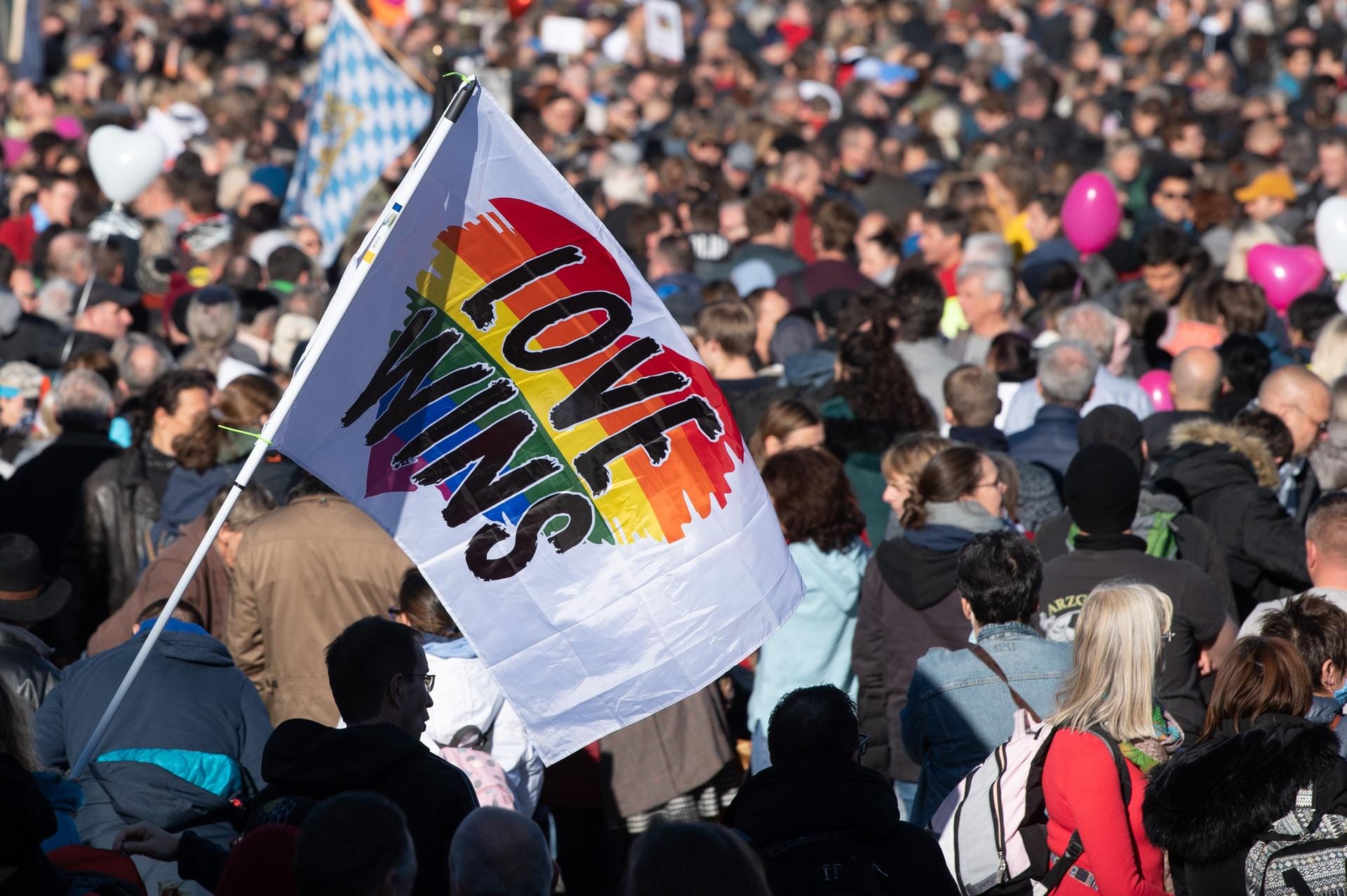 "Love wins" auf einer bunten Fahne: Zahlreiche Teilnehmer stehen dicht an dicht beieinander und tragen keine Maske.