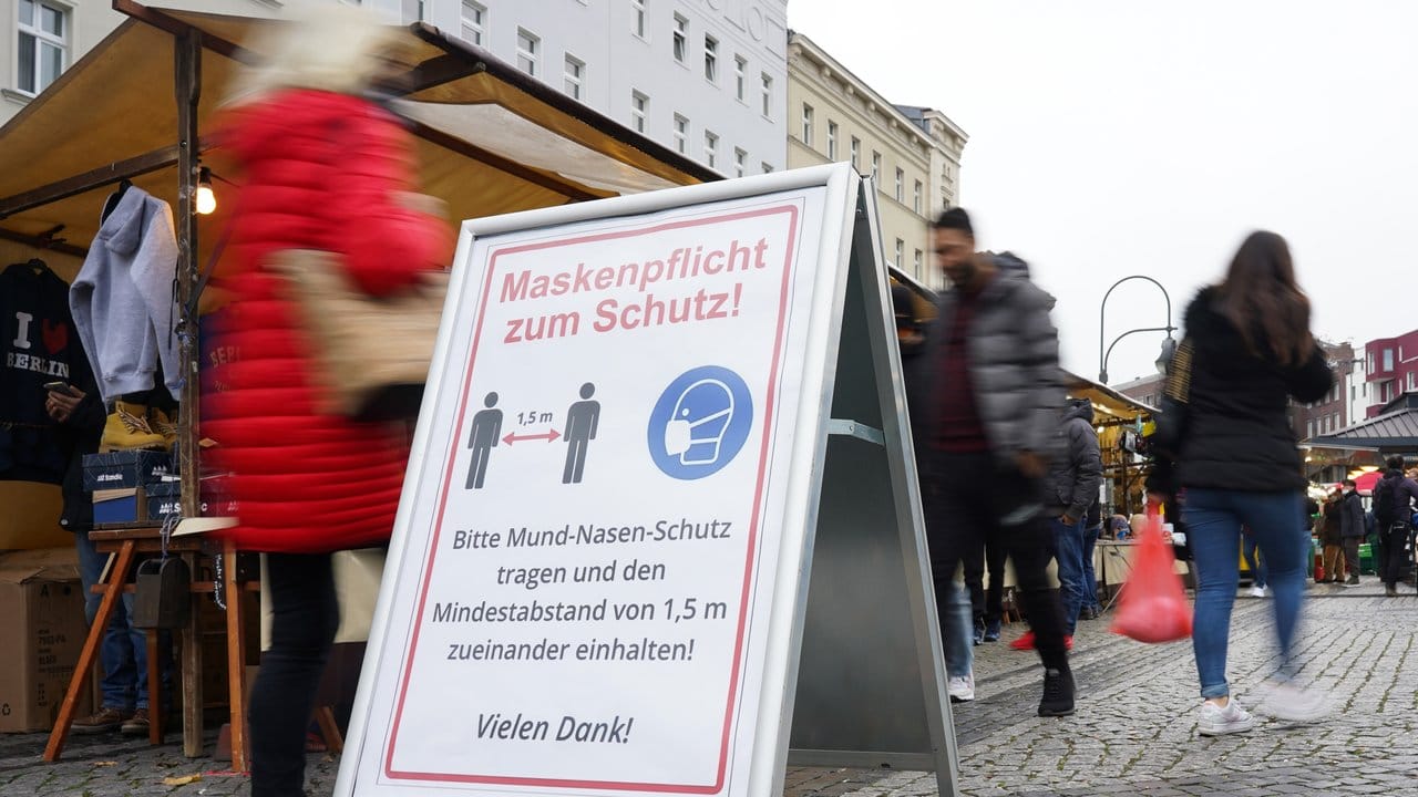 Ein Schild weist auf einem Wochenmarkt in Berlin auf Maskenpflicht und Abstandsgebot hin.