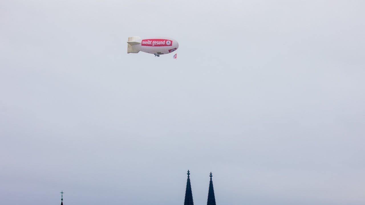 Ein Zeppelin mit der Aufschrift "bliev zohuss" (Bleib zu Hause) der Roten Funken fliegt über den Kölner Dom.
