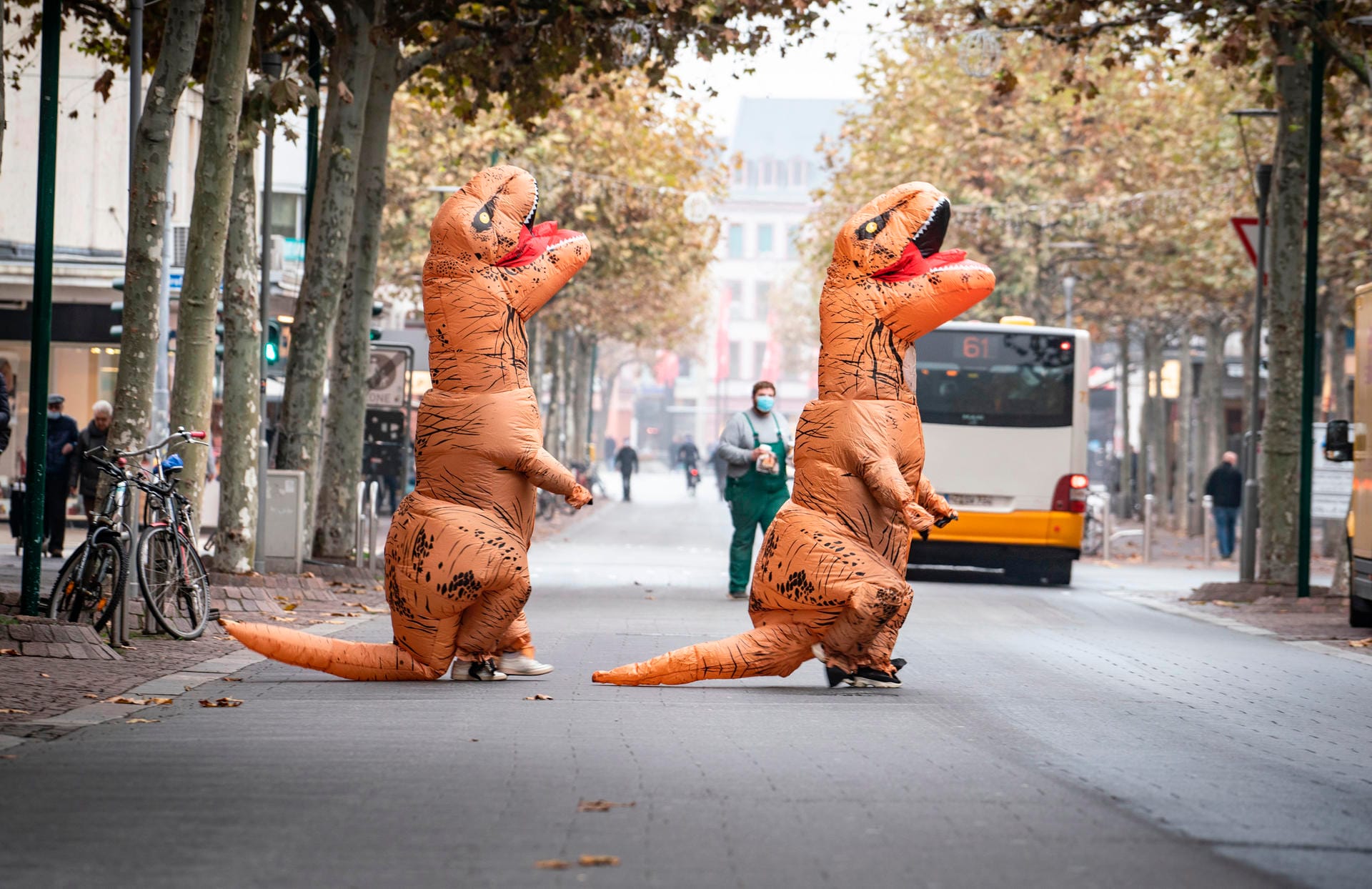 Zwei Karnevalistinnen in aufblasbaren Dinosaurier-Kostümen: Sie überqueren die Straße, die sonst am 11.11. voller Narren ist. Zwei Karnevalistinnen in aufblasbaren Dinosaurier-Kostümen: Sie überqueren die Straße, die sonst am 11.11. voller Narren ist.