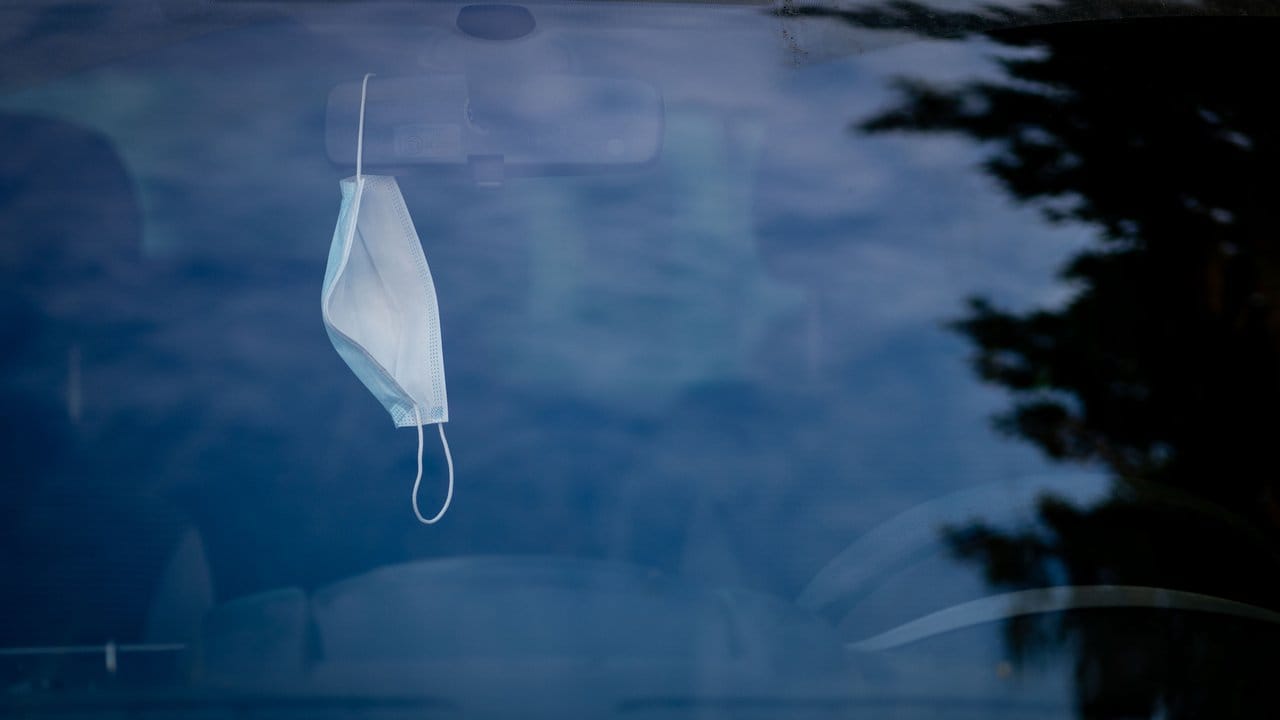 Eine Mund-Nasen-Bedeckung hängt in einem geparkten Auto in Berlin.