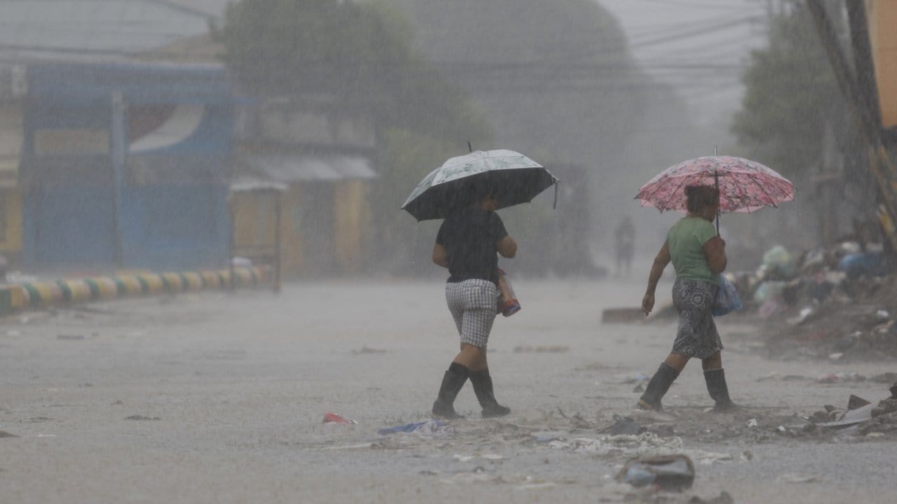 Zwei Frauen überqueren bei starkem Regen eine Straße in La Lima in Honduras.
