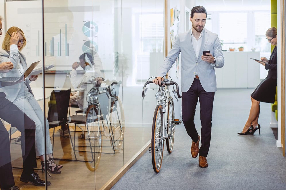 Ein Mann verlässt das Büro mit seinem Fahrrad (Symbolbild): Wer Teilzeit arbeitet, hat früher Feierabend – und Zeit für andere Dinge im Leben.