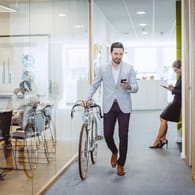 Ein Mann verlässt das Büro mit seinem Fahrrad (Symbolbild): Wer Teilzeit arbeitet, hat früher Feierabend – und Zeit für andere Dinge im Leben.