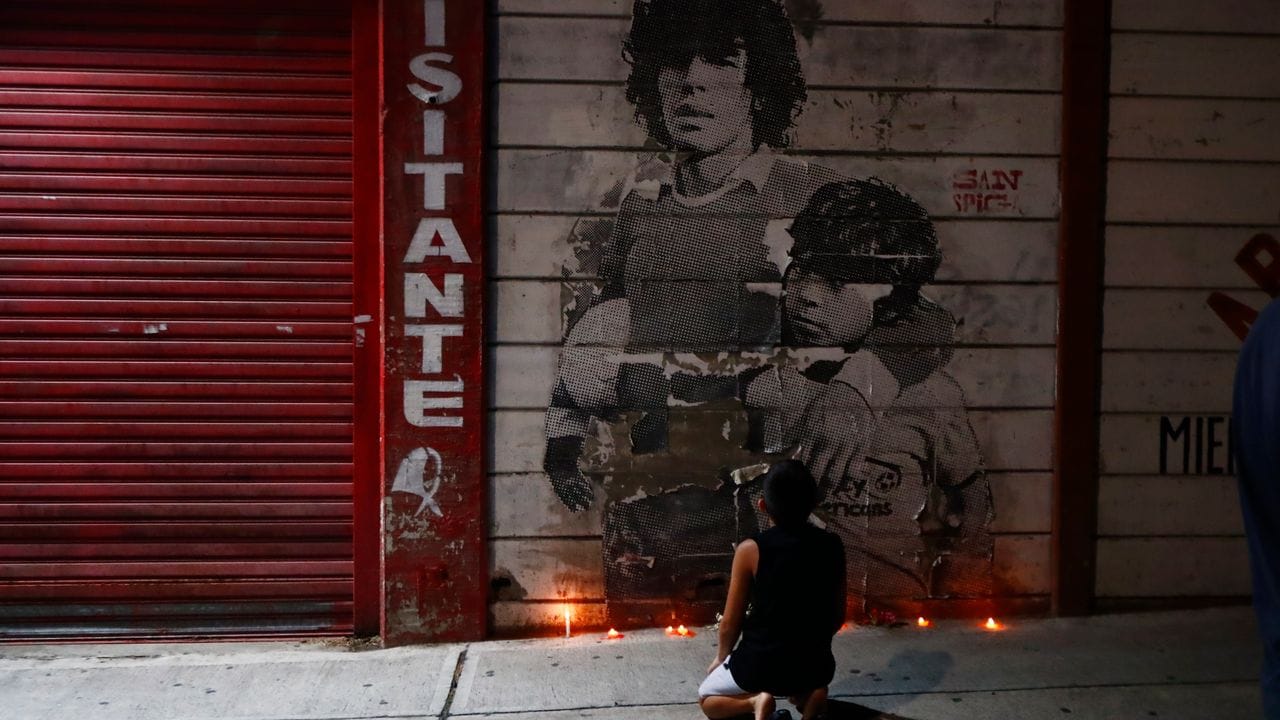 Ein Junge kniet vor einem mit Kerzen dekorierten Wandbild von Diego Maradona in Argentinien.