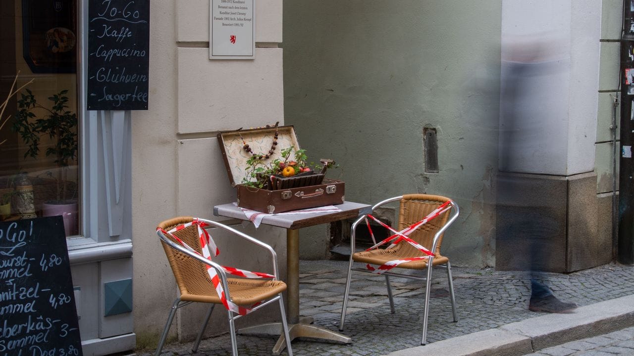 Ein Mann geht an Stühlen eines Cafés vorbei, die mit Flatterband gesperrt wurden. Ein Mann geht an Stühlen eines Cafés vorbei, die mit Flatterband gesperrt wurden.