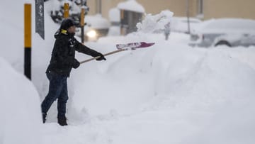 Schweiz, St. Moritz: Ein Mann räumt mit einer Schaufel den gefallenen Schnee von einem Gehweg.
