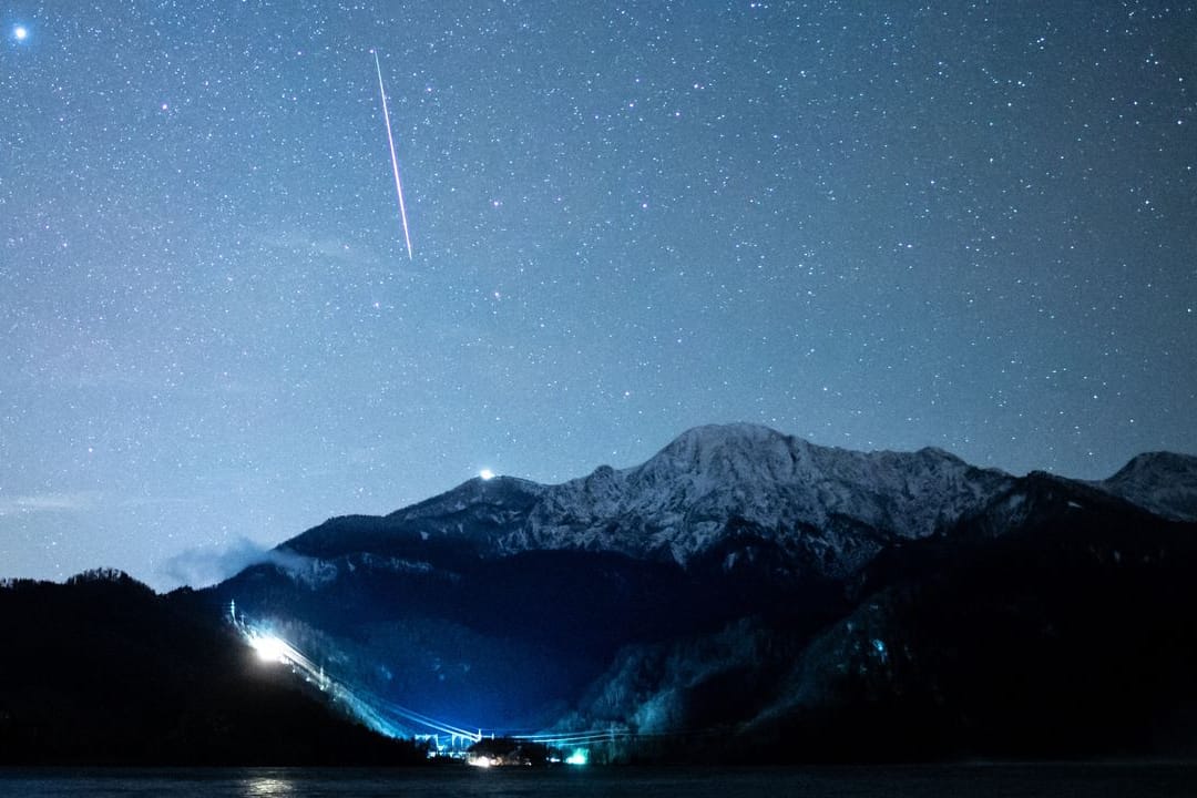 Eine Sternschnuppe ist während des Geminiden-Meteteorstroms am Sternenhimmel über dem Kochelsee zu sehen.