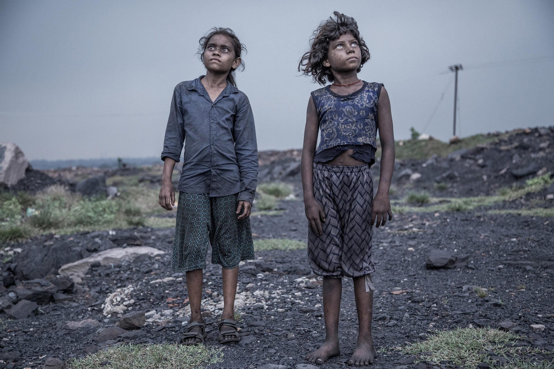 Der indische Fotograf Supratim Bhattacharjee erhielt den zweiten Preis. Sein Bild zeigt zwei Mädchen, unterernährt und erschöpft. Sie sind zwei von vielen Kindern, die auf Asiens größten Kohlefeldern arbeiten. Diese liegen in Jharia im indischen Bundesstaat Jharkhand. Am Ende des Tages erhalten die Mädchen für ihre Arbeit einen Lohn von umgerechnet zwei US-Dollar. Genügend Nahrung, sauberes Trinkwasser oder gar Schulbildung bekommen sie davon nicht.