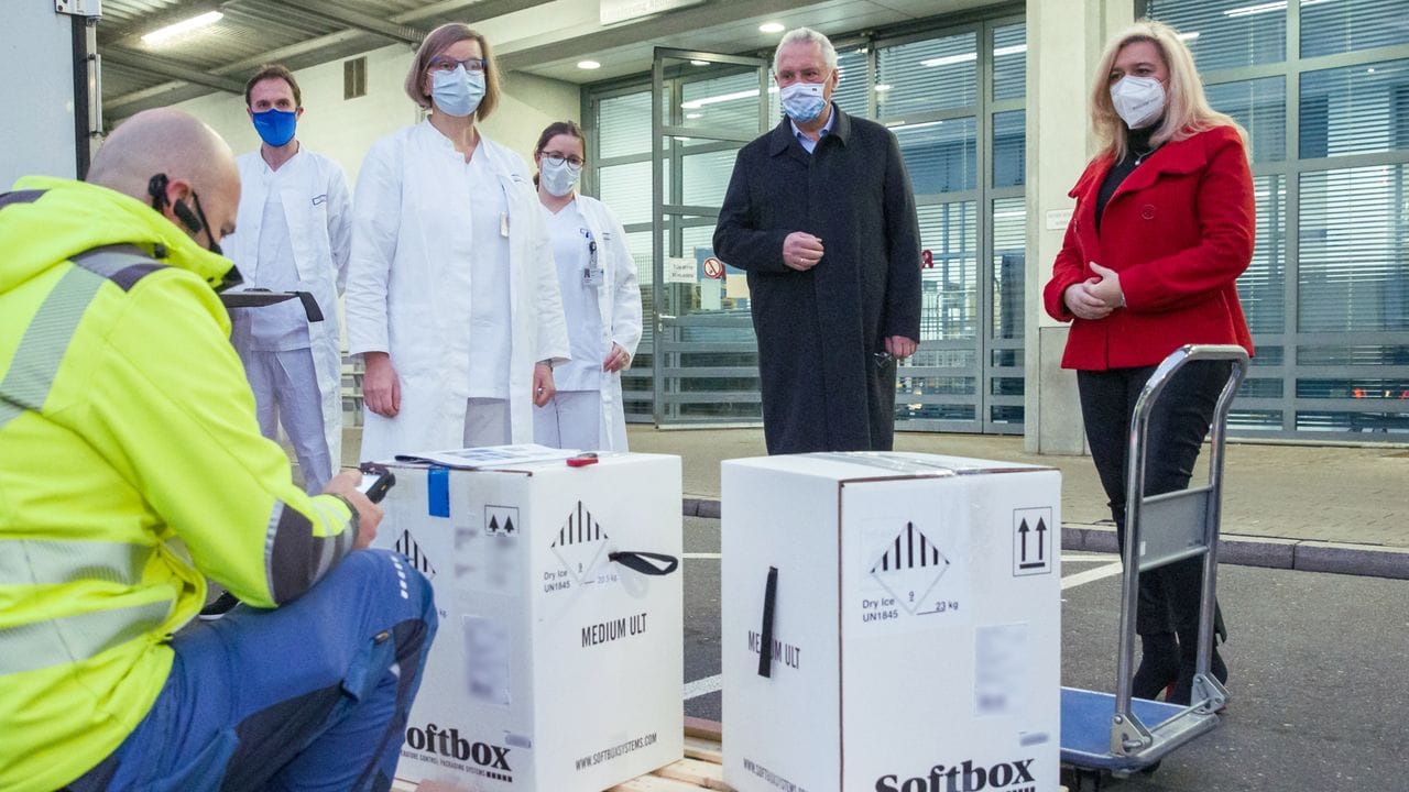 Bayerns Innenminister Joachim Herrmann (M) und Gesundheitsministerin Melanie Huml stehen in Erlangen neben Kartons mit den ersten Impfstoffdosen für Bayern.