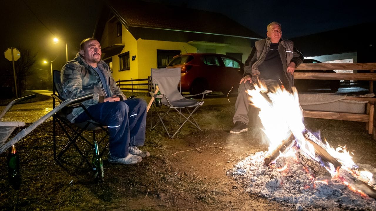 Zwei Männer sitzen neben einem Lagerfeuer, während sie aufgrund der Gefahr von Nachbeben die Nacht im Freien verbringen.