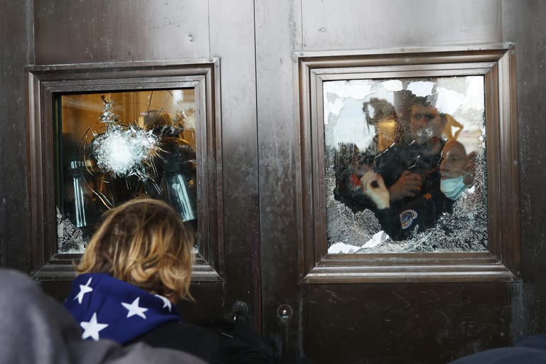 Polizisten hinter zertrümmerten Fensterscheiben, Protestierende versammeln sich vor dem Eingang des Kapitols.