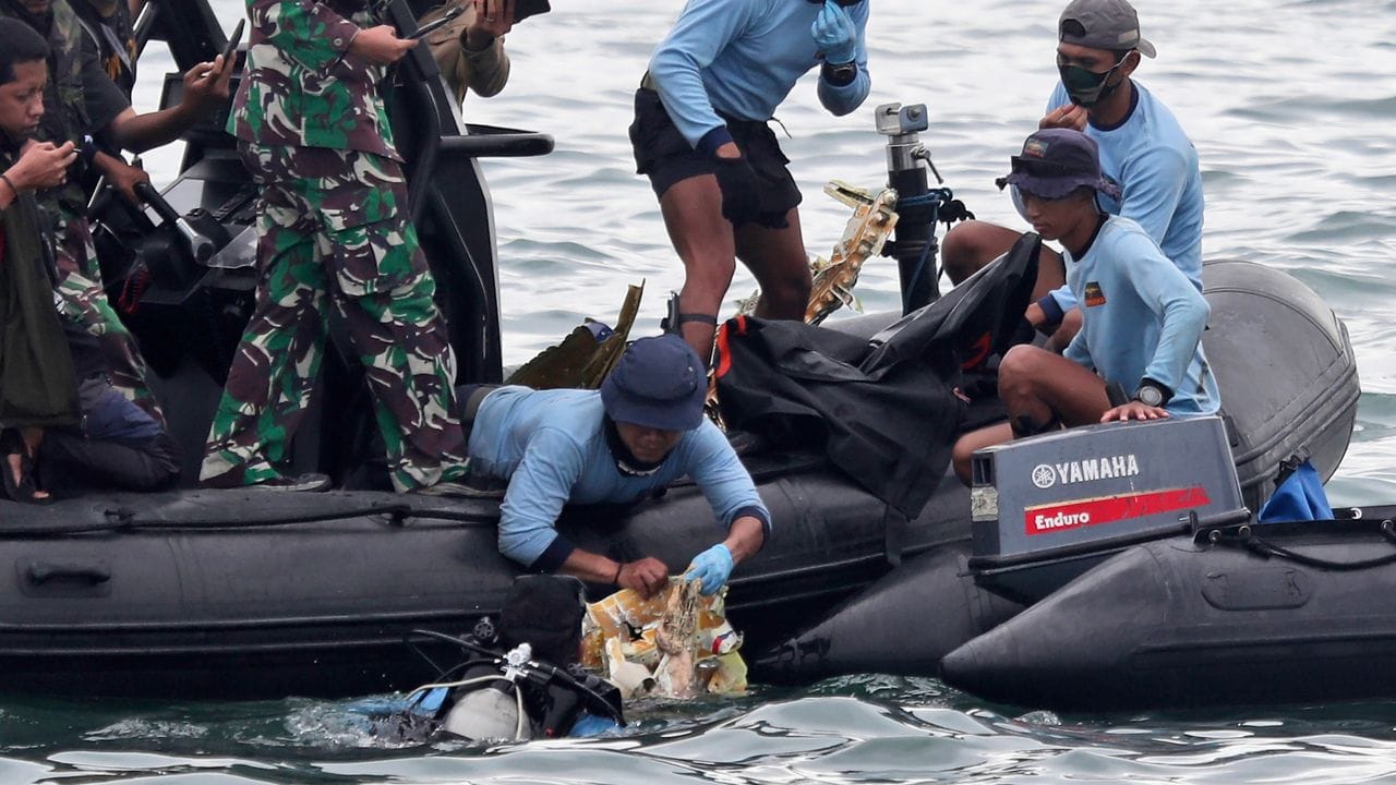 Taucher der indonesischen Marine ziehen ein Flugzeugteil aus dem Wasser.