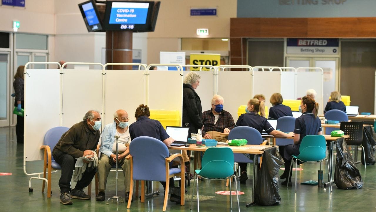 Menschen, die sich gegen das Coronavirus impfen lassen wollen, sitzen zusammen mit Mitarbeitern im NHS-Impfzentrum in Epsom.