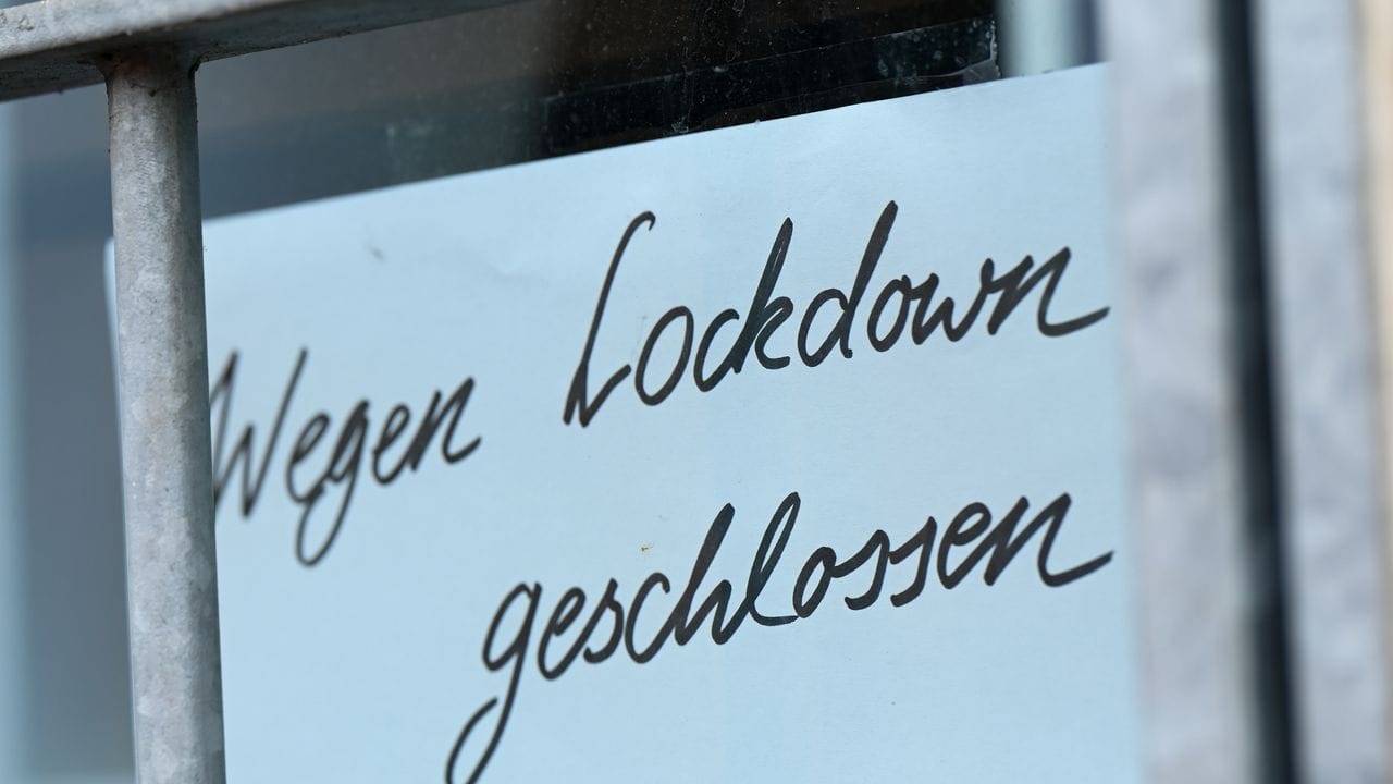 Ein Zettel mit der Aufschrift "Wegen Corona geschlossen" hängt am Schaufenster eines Geschäfts.