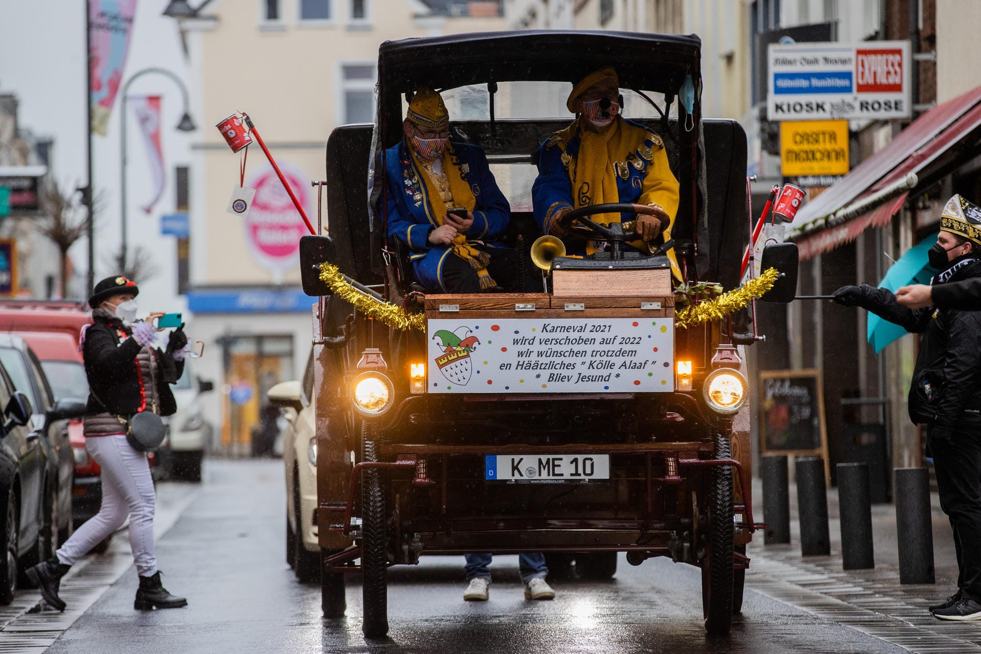 Karnevalisten fahren mit einem historischen Fahrzeug auf der Severinstraße. Darauf ist die Aufschrift zu lesen: "Karneval 2021 – wird verschoben auf 2022 – wir wünschen trotzdem en Häätzliches Kölle Alaaf - Bliev Jesund".