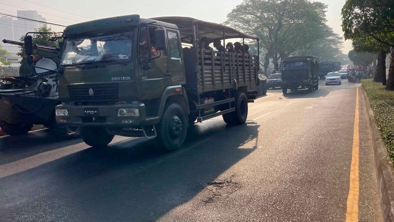 Ein Konvoi von Militärlastwagen mit Soldaten fährt in Rangun an gepanzerten Militärfahrzeugen vorbei.