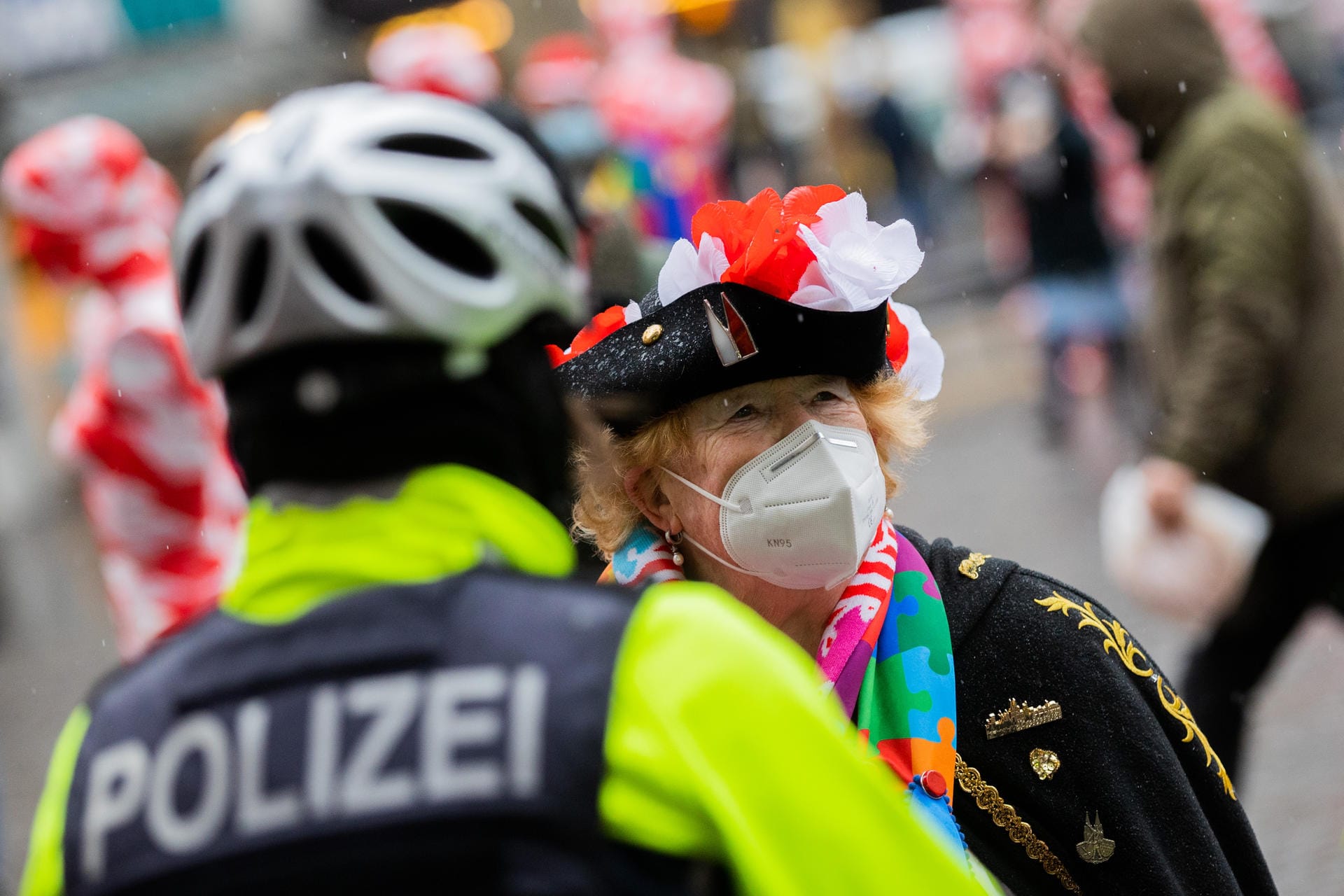 Polizeibeamte unterhalten sich mit einer Jeckin am Severinstor. In diesem Jahr müssen die Jecken mit zusätzlicher Maske den Rosenmontag begehen.