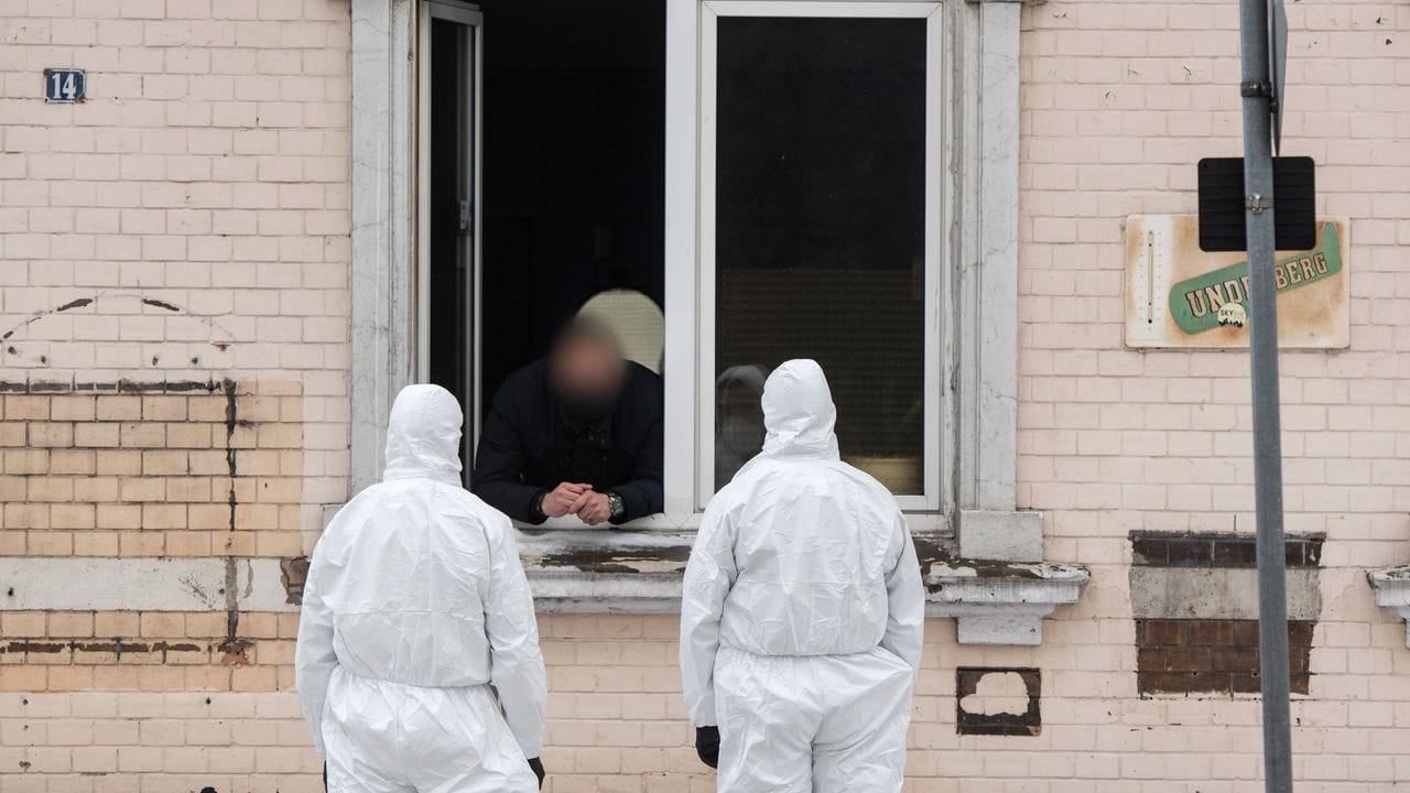 Einsatzkräfte der Polizei unterhalten sich durch ein Fenster mit einem Mann.