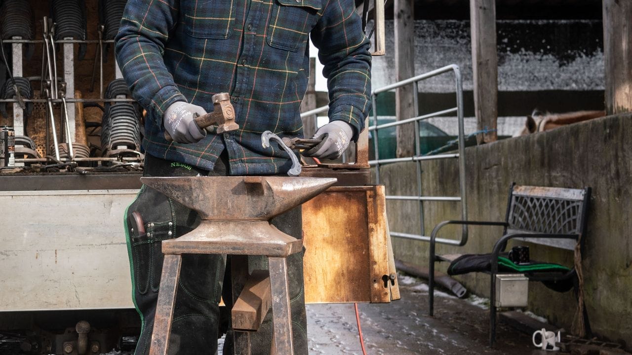 Der angehende Hufschmied Tim Bishop bearbeitet das glühende Eisen auf dem Amboss mit dem Hammer.