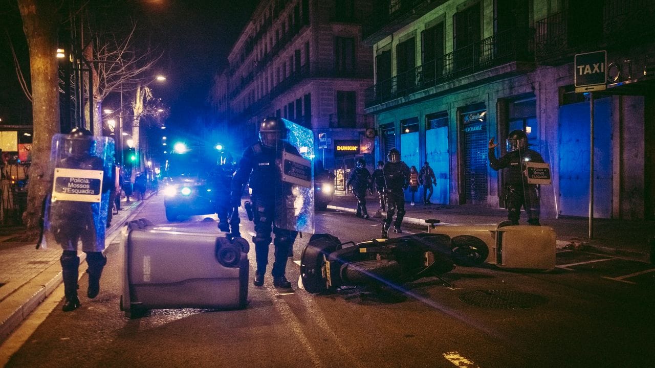 Katalanische Bereitschaftspolizei gehen in Barcelona eine Straße entlang, auf der Protestler Mülltonnen und einen Motorroller umgekippt haben.