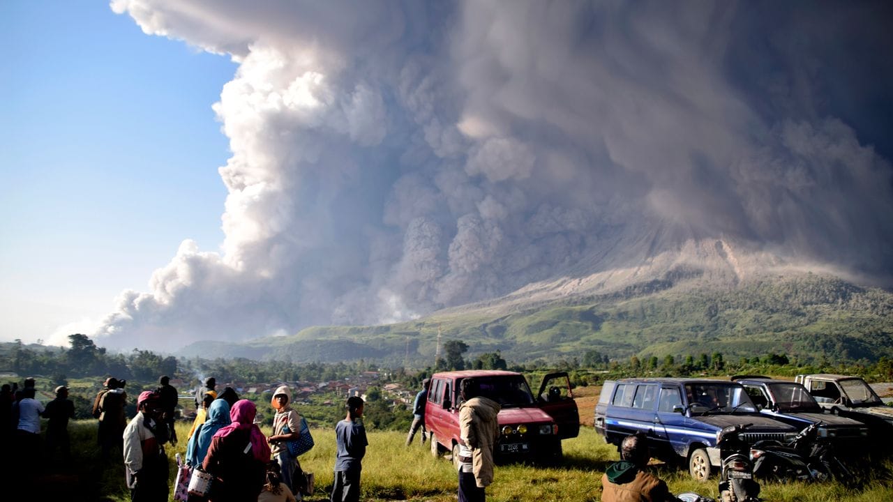 Menschen beobachten eine Eruption des Vulkans Sinabung.