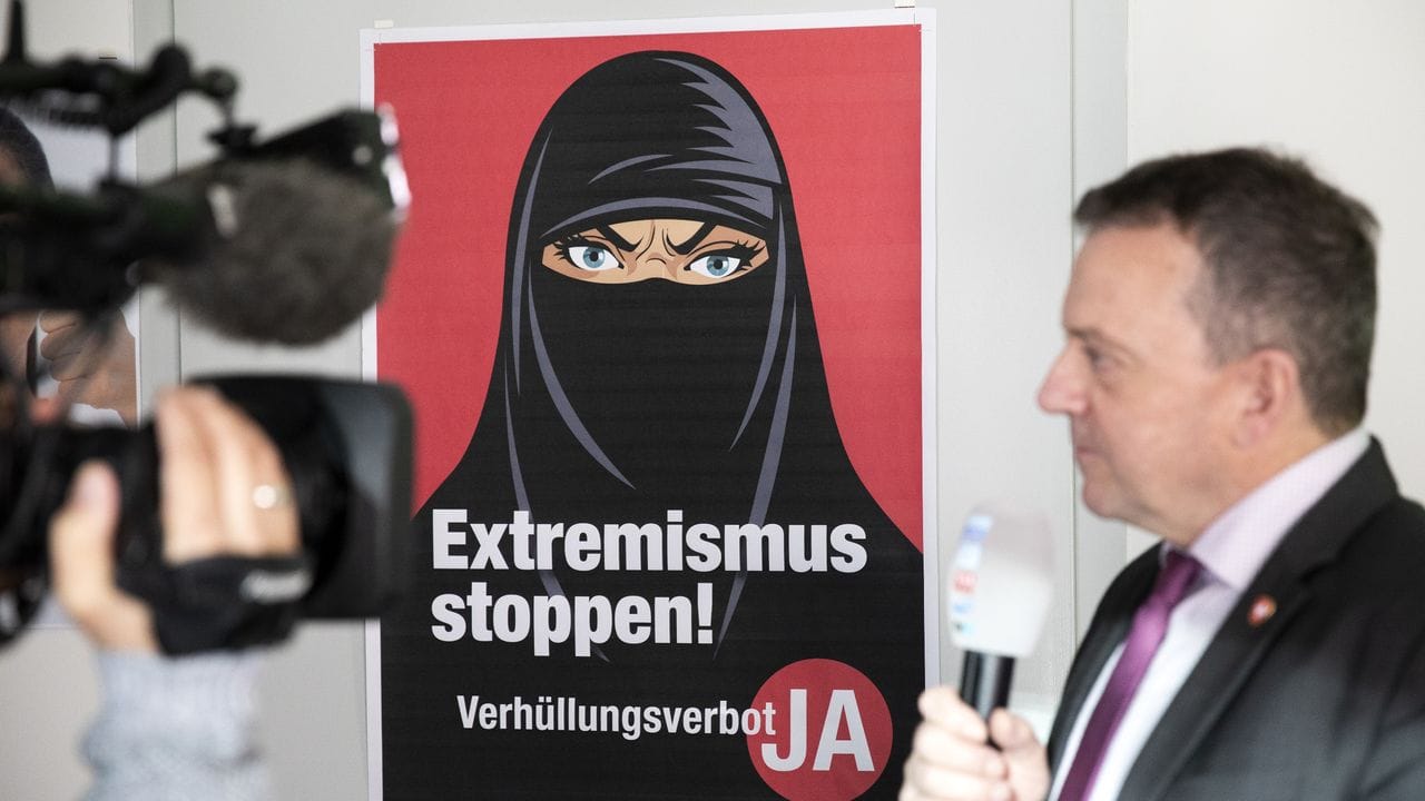 Walter Wobmann, Initiator der Initiative "Ja zum Verhüllungsverbot", gibt neben einem Plakat mit der Aufschrift "Extremismus stoppen" ein Interview.