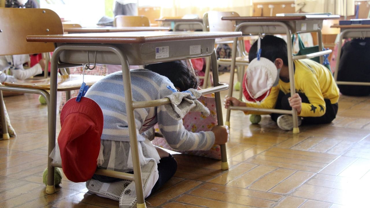 Grundschüler suchen während einer Erdbeben-Notfallübung in Usuki Schutz unter ihren Tischen.