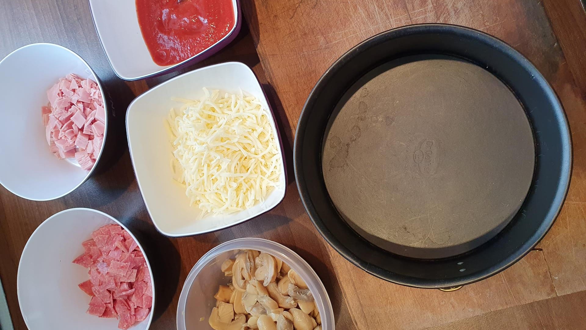 Backen Sie die Pizzaböden im Ofen für fünf Minuten vor. Nehmen Sie dann den ersten vorgebackenen Pizzateig und legen ihn unten in die Springform.